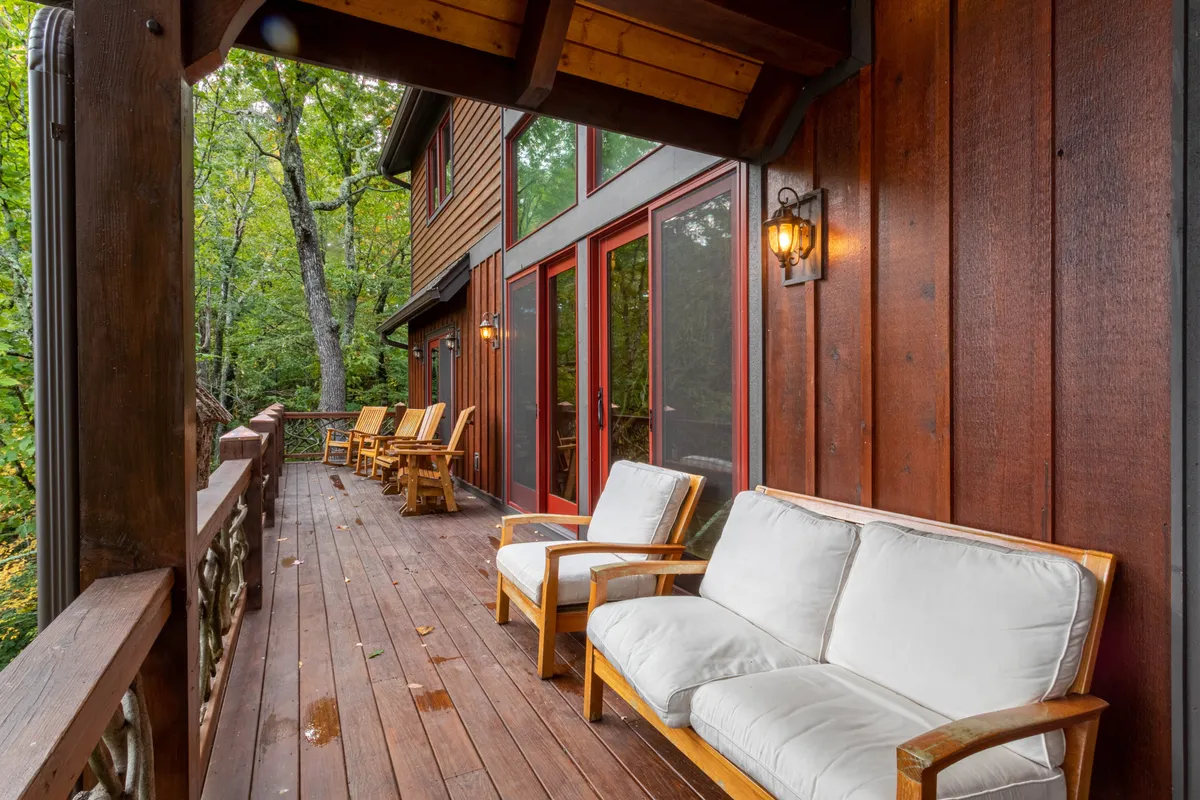 This image captures a wooden deck surrounded by lush trees, with comfortable seating and large windows suggesting a seamless indoor-outdoor flow. The tranquil setting emphasizes privacy, relaxation, and immersion in nature—core qualities of an exclusive mountain escape.
