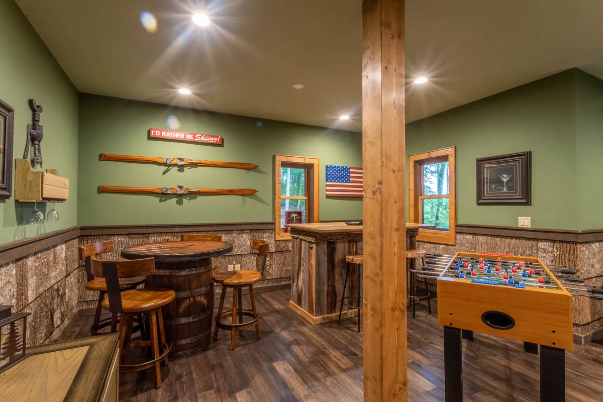 A lively game room setting with a foosball table, rustic bar area, and wooden beams creating a playful, communal vibe. The American flag and bar seating add to the casual, festive atmosphere, suggesting a space for both games and socializing.