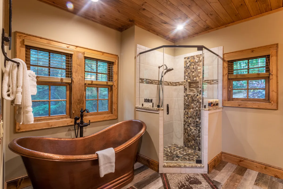 A spa-like bathroom centered on a freestanding hammered copper bathtub, complemented by a glass shower enclosure and wooden window frames. The space feels tranquil, elegant, and rejuvenating, embodying indulgent self-care.