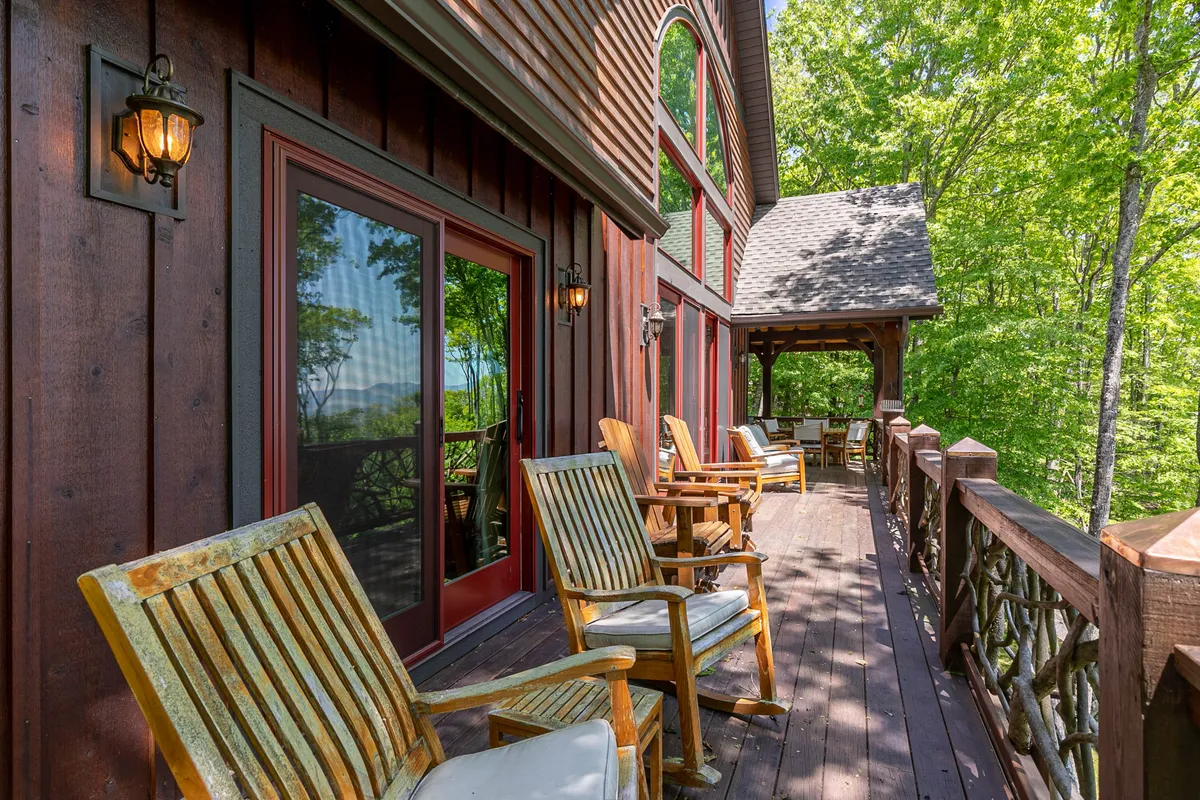 A tranquil wooden deck with classic rocking chairs overlooks a lush, tree-filled yard. The deck is surrounded by nature and invites guests to relax while keeping an eye on pets playing safely in the fully fenced yard below.