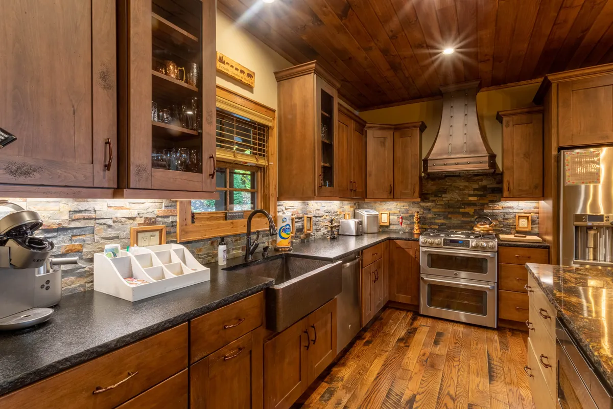 The image highlights a beautiful kitchen with granite countertops, a farmhouse sink, stone backsplash, wooden cabinetry, and sleek stainless steel appliances. The cozy, welcoming atmosphere makes it perfect for preparing meals with family or friends.