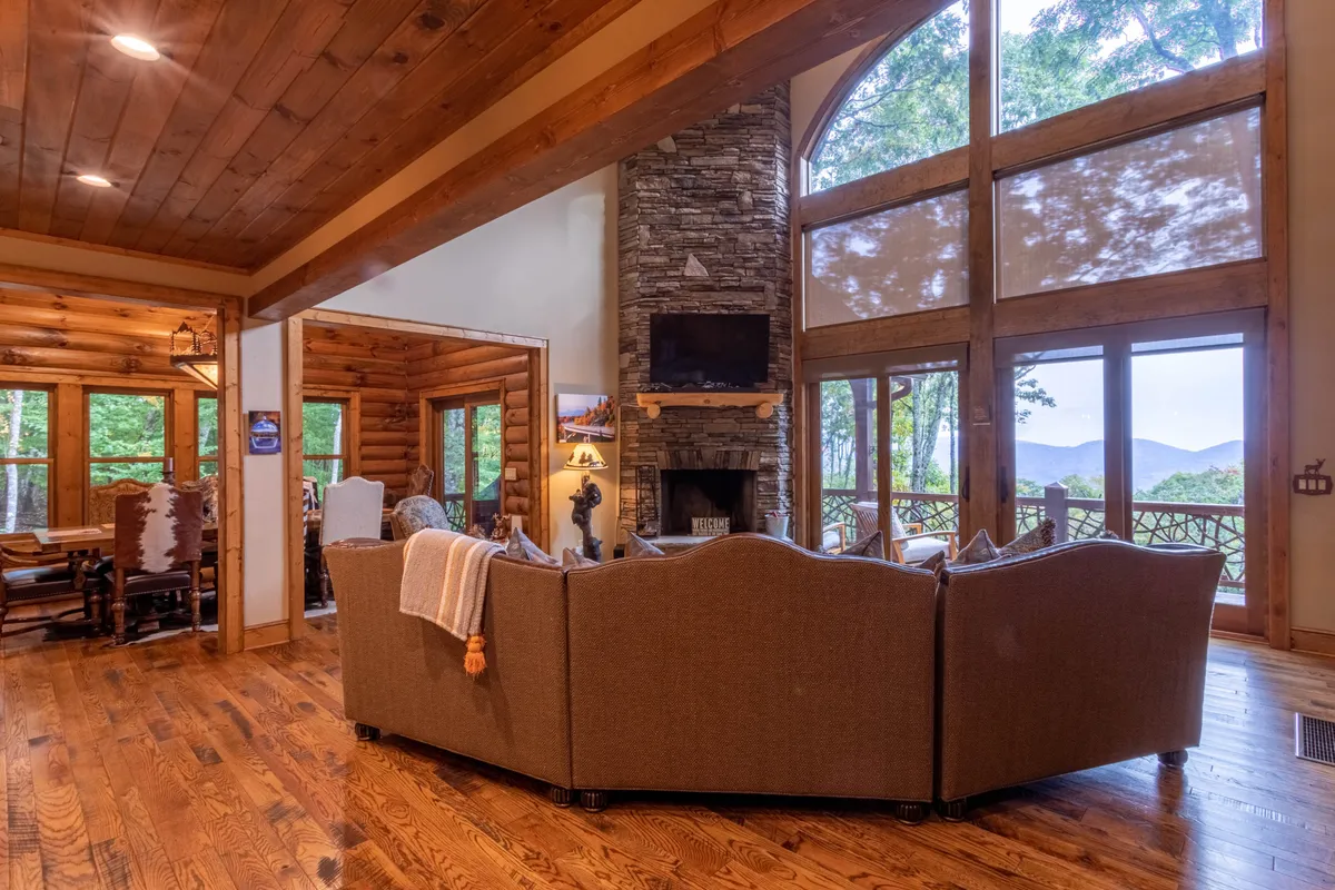 A spacious living area with a prominent stone fireplace, expansive windows offering stunning mountain views, and plush seating ideal for family gatherings or movie nights. The natural wood accents echo the region’s mountain aesthetic.