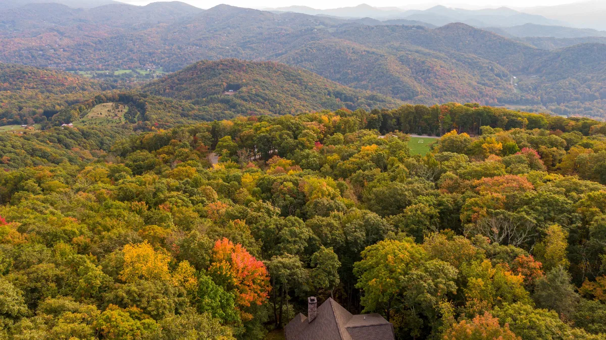 A sweeping view of a vibrant mountain range with brilliant autumn foliage, with the rooftop of the house visible in the foreground. The scene suggests tranquility and the allure of nature, hinting at the proximity of trails and the stunning views guests can enjoy from the property.