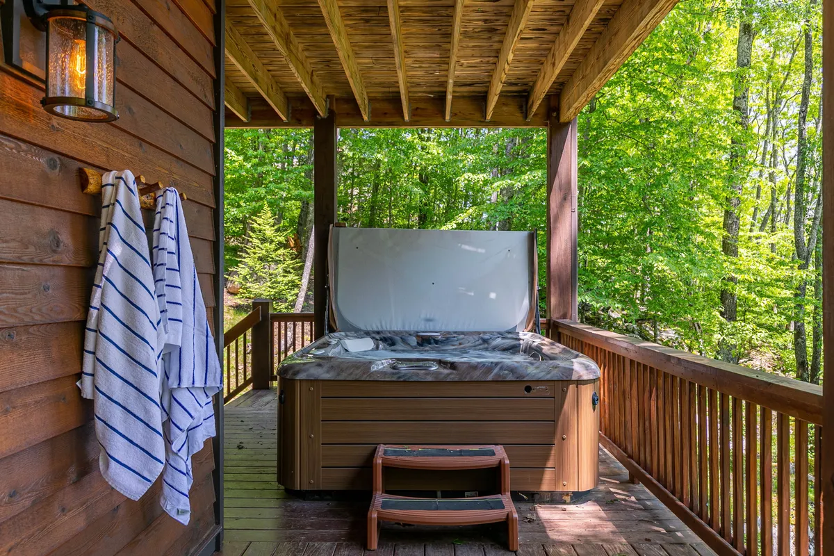 An outdoor hot tub situated on a wooden deck, with hanging towels and ample space for a group to relax. The setting is surrounded by trees, creating a sense of privacy and immersion in nature—ideal for unwinding after a day of exploration or enjoying an evening soak with friends.