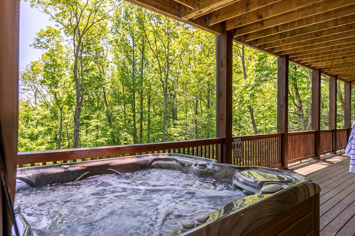 A wooden deck features a luxurious hot tub set amid lush greenery, offering a secluded spot for relaxation and wellness. The natural surroundings evoke a sense of serenity and exclusive indulgence.