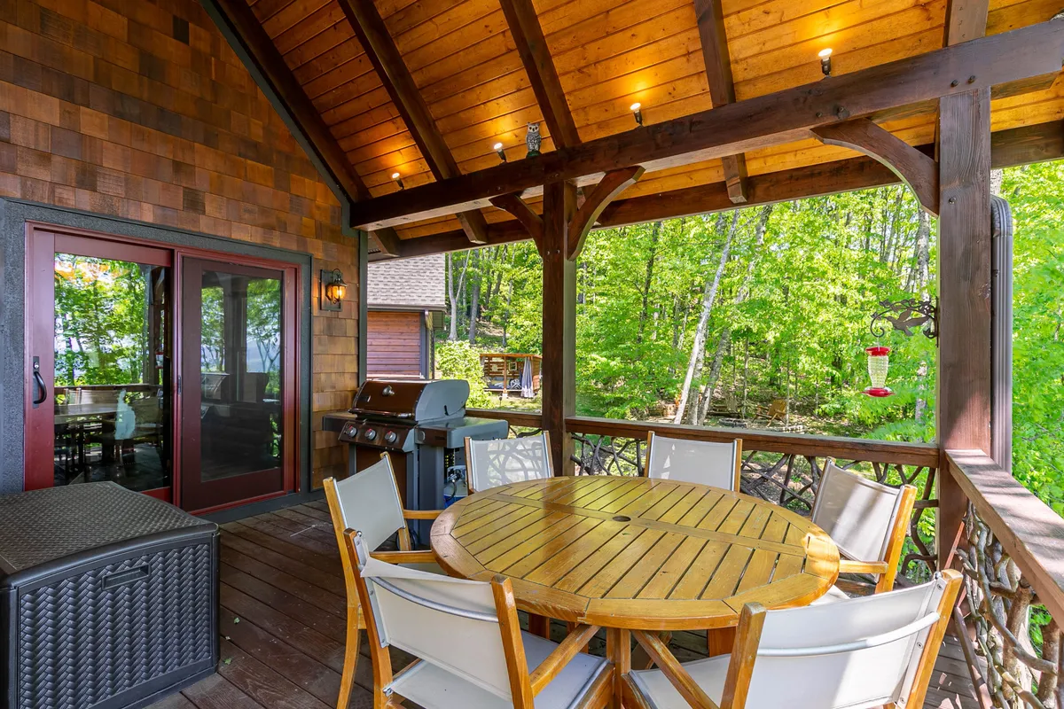 An inviting outdoor dining area featuring a wooden table and grill set amidst lush greenery. Comfortable dining chairs are arranged for a group, perfect for sharing a meal or drinks in a relaxed, natural setting. The sunset light gives the space a warm, sociable atmosphere.