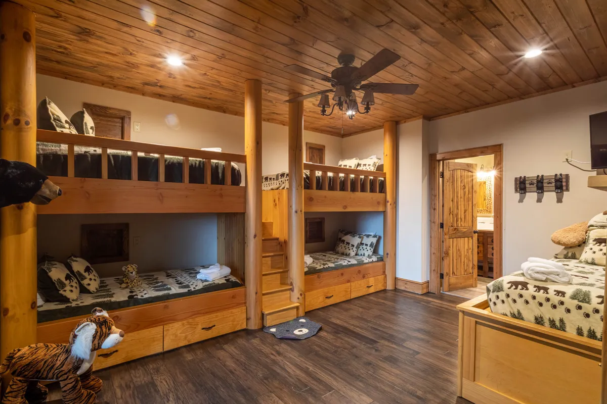 A cozy bunkroom with wooden bunk beds, playful stuffed animals, a wood-paneled ceiling, and a ceiling fan. The design encourages imaginative play and togetherness for young guests.