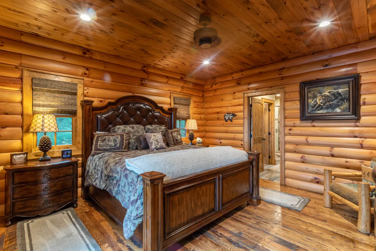 A warmly lit bedroom featuring a wooden bed with plush bedding, lamps on nightstands, a large wooden dresser, and inviting artwork on the wall. The room radiates comfort and tranquility, with natural light filtering in.
